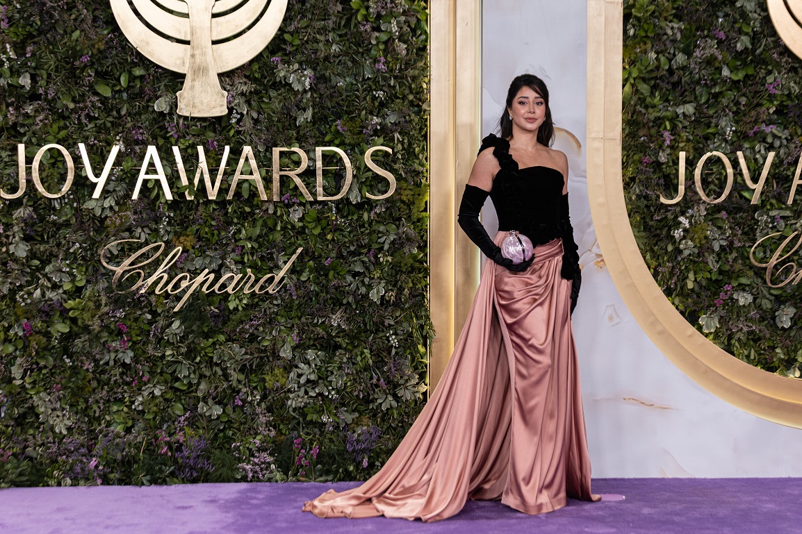 أسيل عمران بفستان بقماش المخمل الأسود مزين بحمالة مائلة من الورود الممتدة