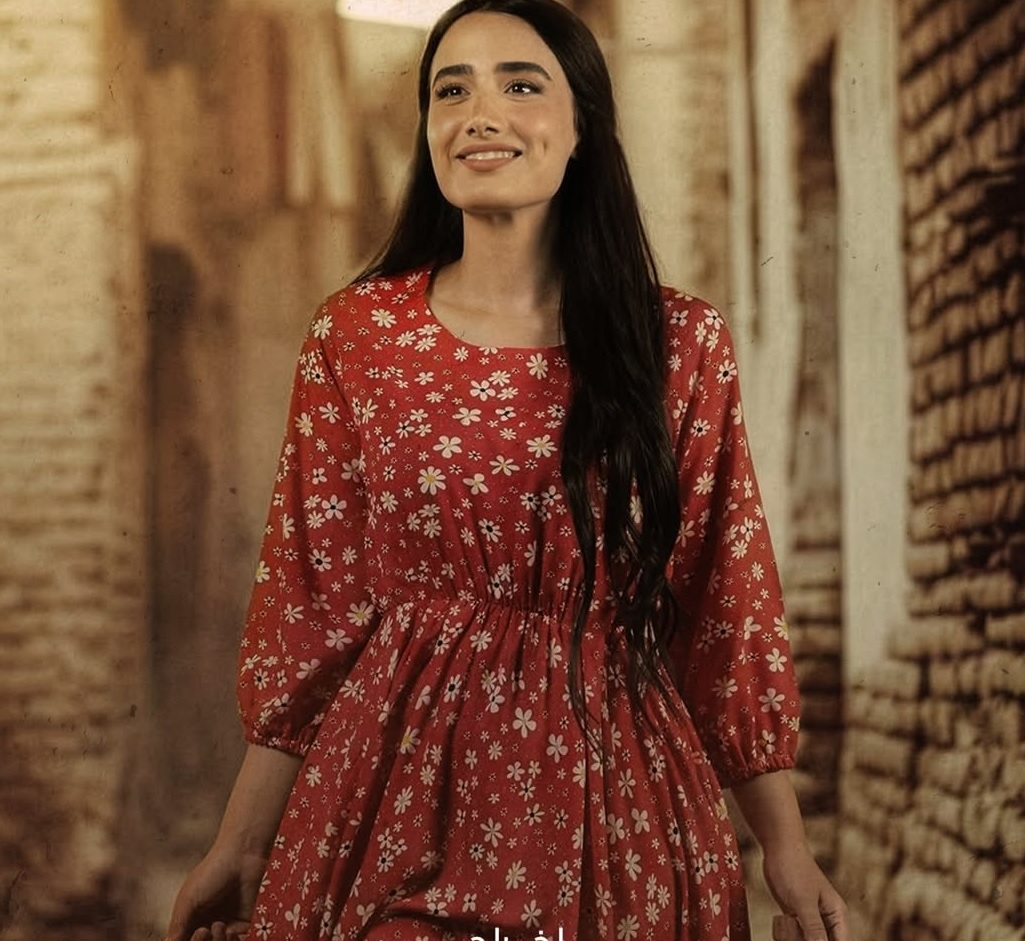 أميمة جواد الشكرجي على بوستر المسلسل بإطلالة أنثوية ناعمة، بستايل فستان طويل باللون الأحمر، تزينه طبعة الورود