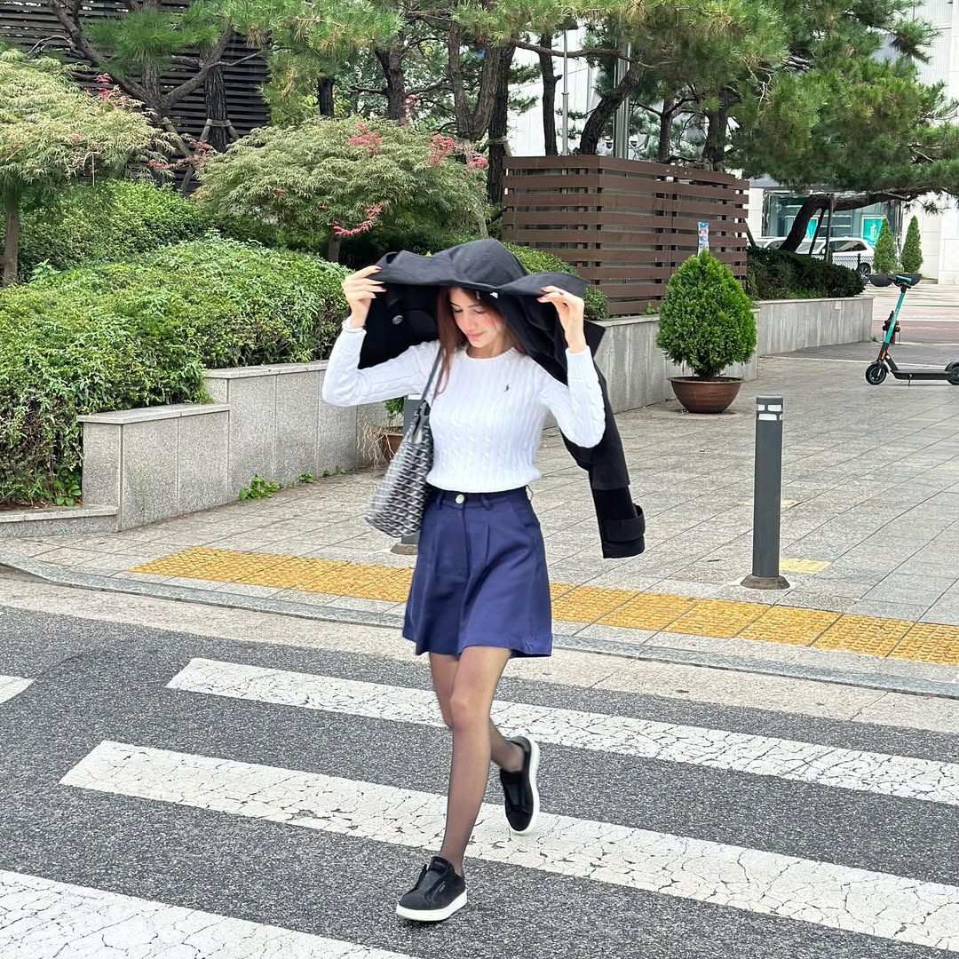 سيدرا عمارة ببلوفر أبيض بأكمام طويلة مع تنورة كلاسيكية قصيرة باللون الأزرق 