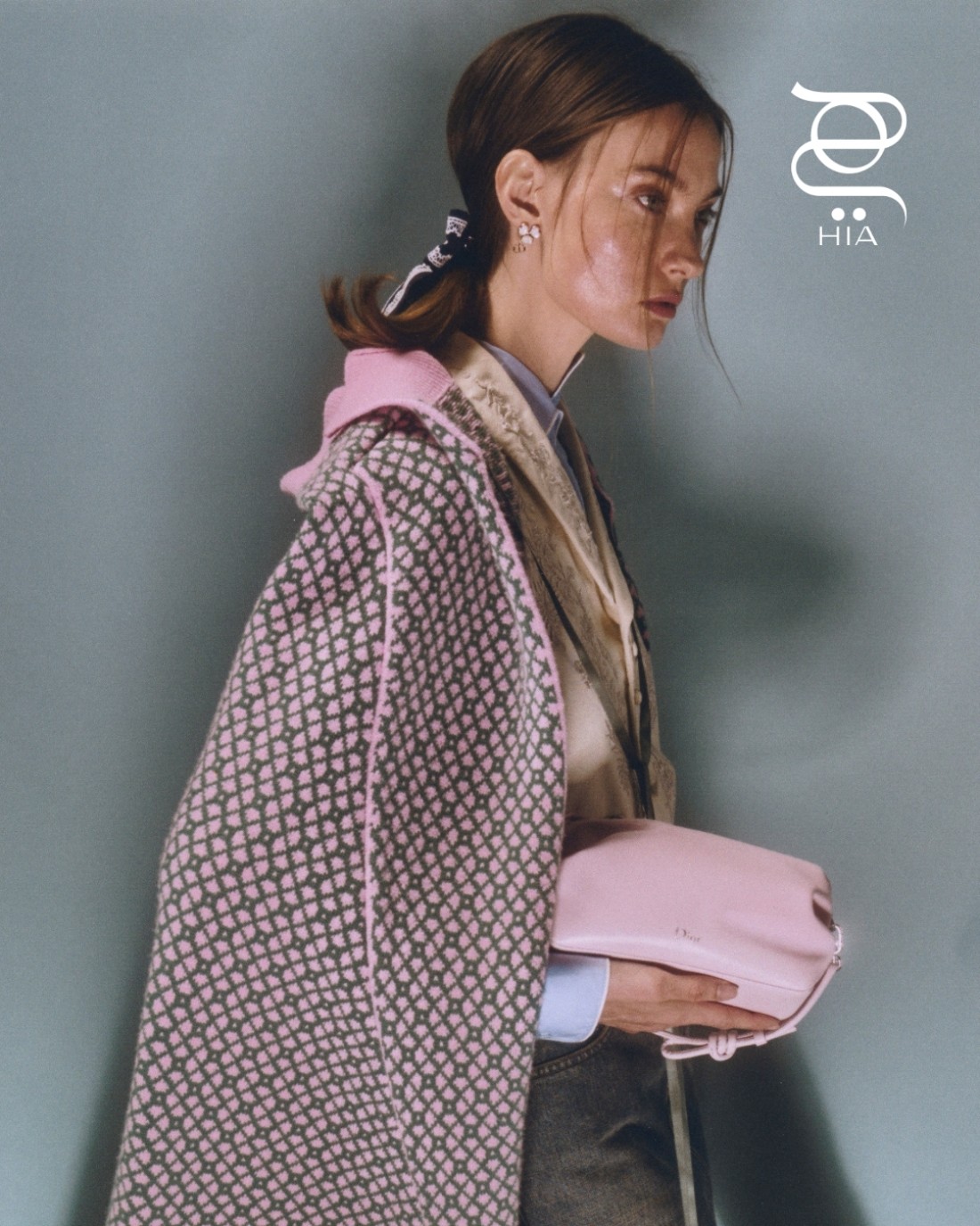 أقراط وبكلة "تويست بوو" ‏Twist Bow قميص أزرق وسترة باللون البيج ‏ مع كاب مزدان بنقشات زهرية وخضراء سروال دنيم وحقيبة كلاتش ‏ ‏"ديور بوو" ‏Dior Bow‏ باللون الزهري ‏ جميعها من دار "ديور" ‏Dior