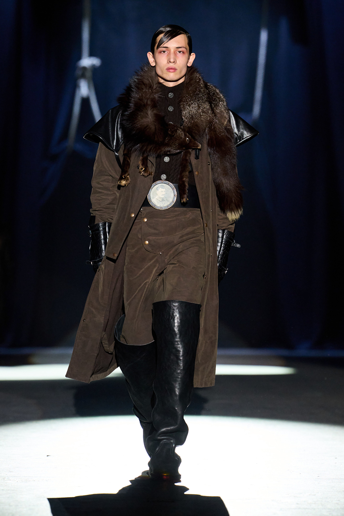 حذاء طويل باللون الأسود من Enfants Riches Déprimés نُسق مع إطلالة من الشامواه باللون البني الكاكي، في تناغم يعكس ذوقًا جريئًا وراقيًا في آن واحد