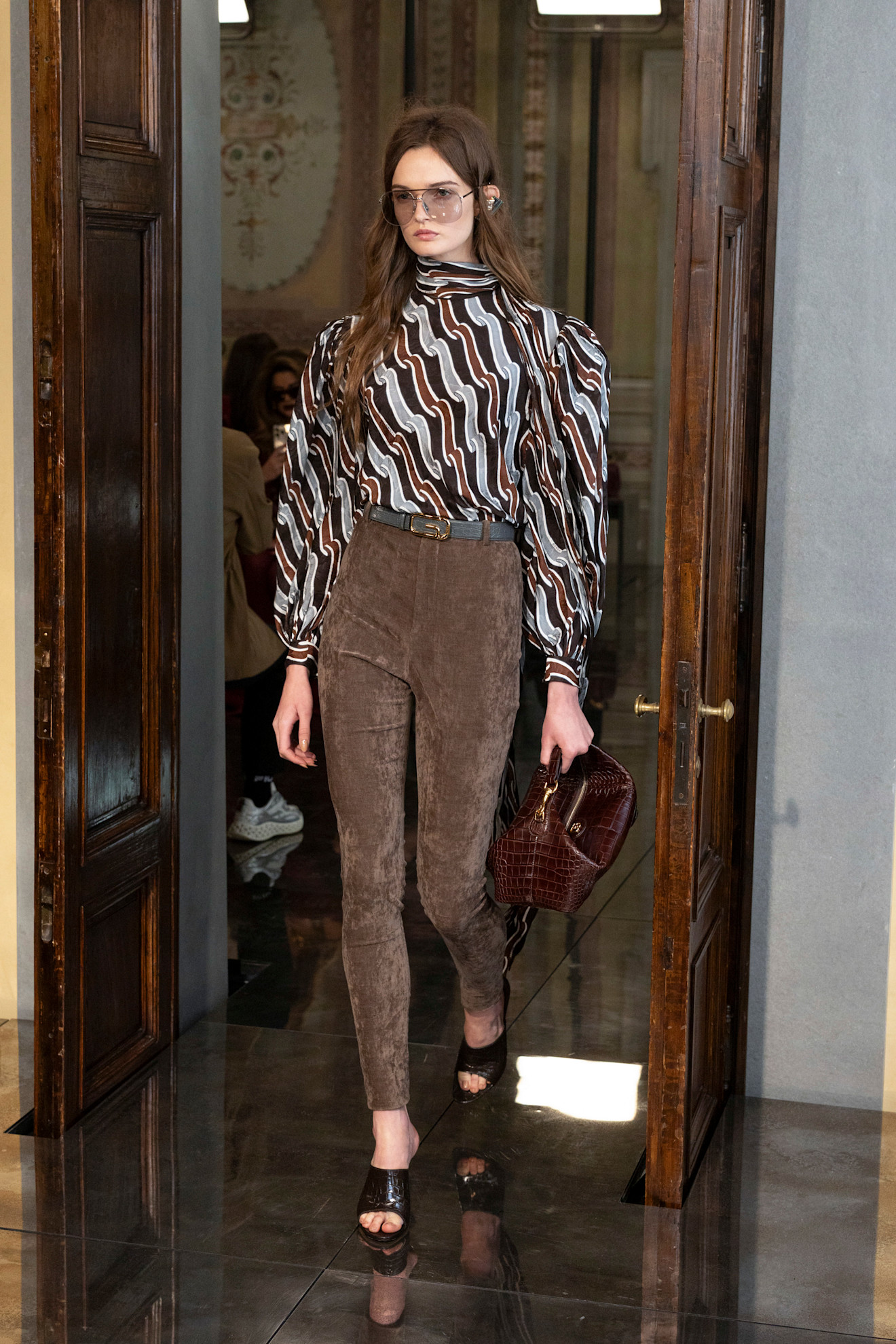 سروال ضيق من الفلور البني من غوتشي، منسّق مع قميص بنقشة فينتاج، لإطلالة غنية بالتفاصيل وتوازن بين الماضي والحاضر