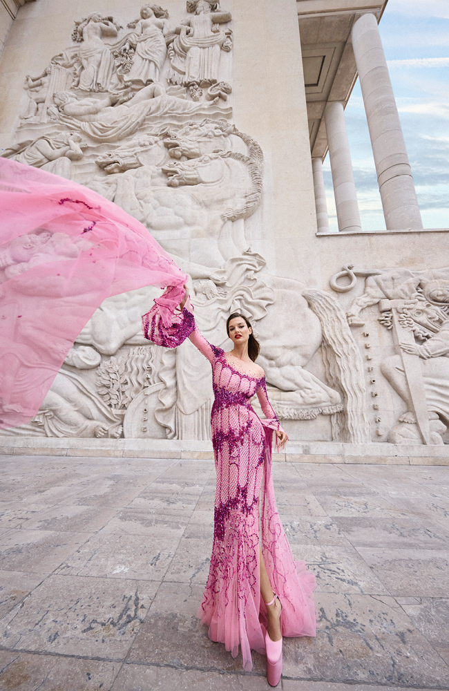 من "جورج حبيقة هوت كوتور"Georges Hobeika Haute Couture، فستان ليلكي طويل مطرز بتفاصيل أرجوانية ومصمم بكمّين يلامسان الأرض، وحذاء ليلكي اللون ذو نعل سميك.