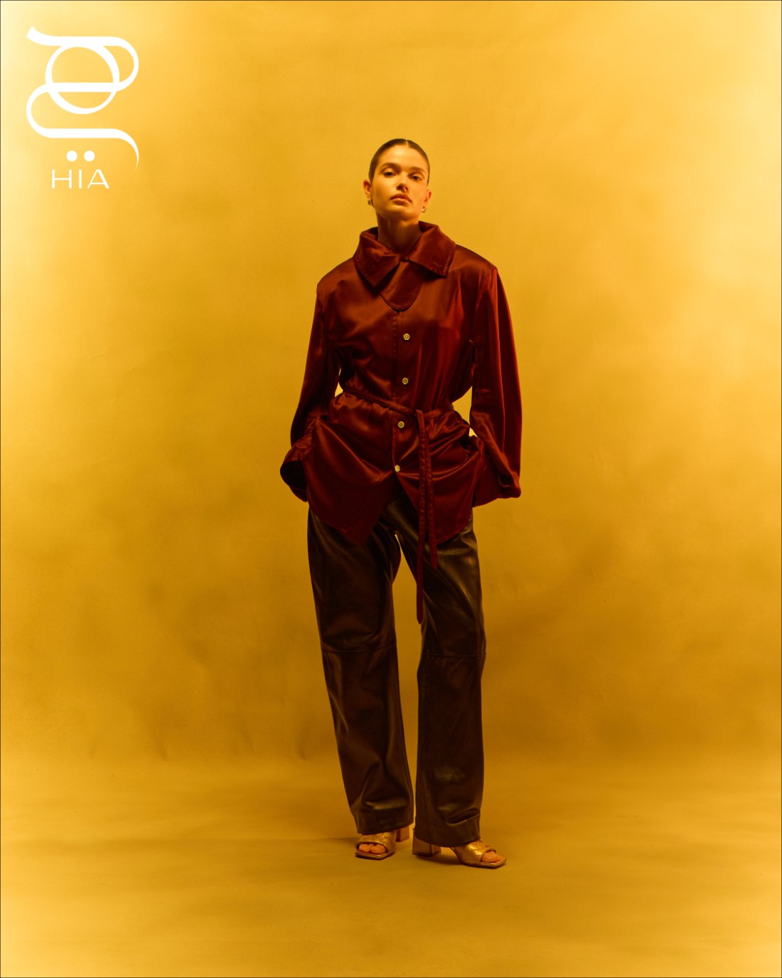 قميص حريري مع حزام باللون العنابي وسروال أسود ‏ حذاء ميول "باركو" ‏PARCO‏ باللون الذهبي ‏ جميعها من دار "بوتيغا فينيتا" ‏Bottega Veneta