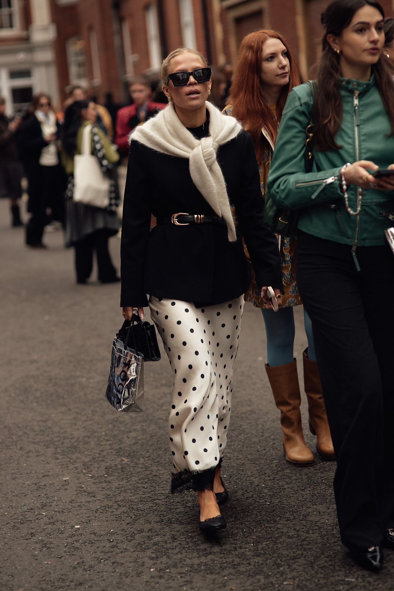 تنورة ساتان مرقطة مع أطراف الدانتيل الأسود، نُسقت مع سترة بلايزر كلاسيكية ووشاح على الكتفين لإطلالة تجمع بين الرقي والمرح.