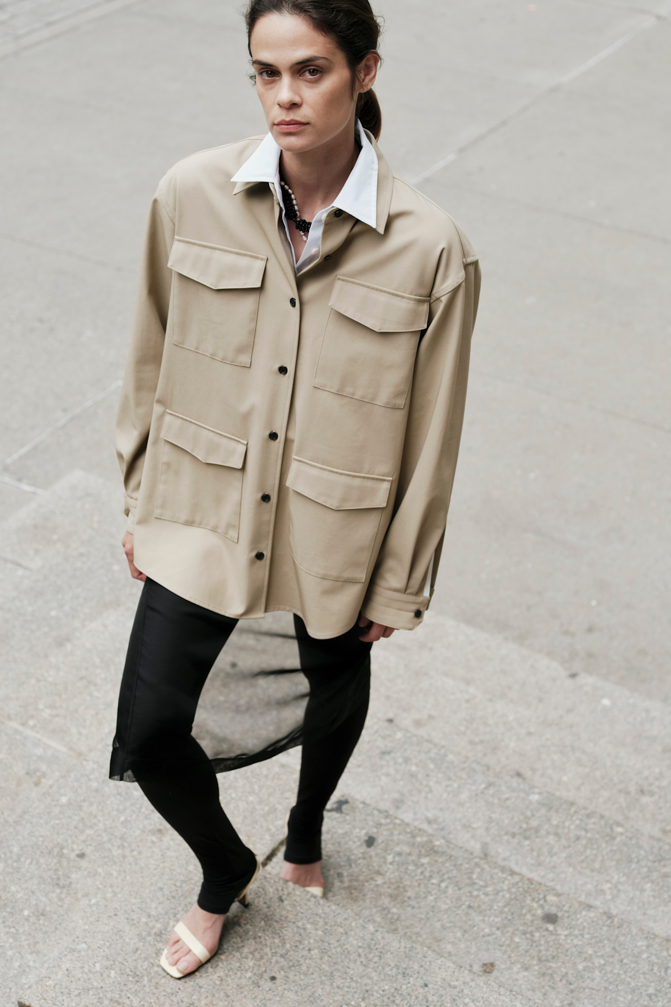 سروال أسود ضيق من ماريا مكمانوس، منسّق مع قميص بأسلوب عسكري باللون البيج، لإطلالة تجمع بين القوة والبساطة