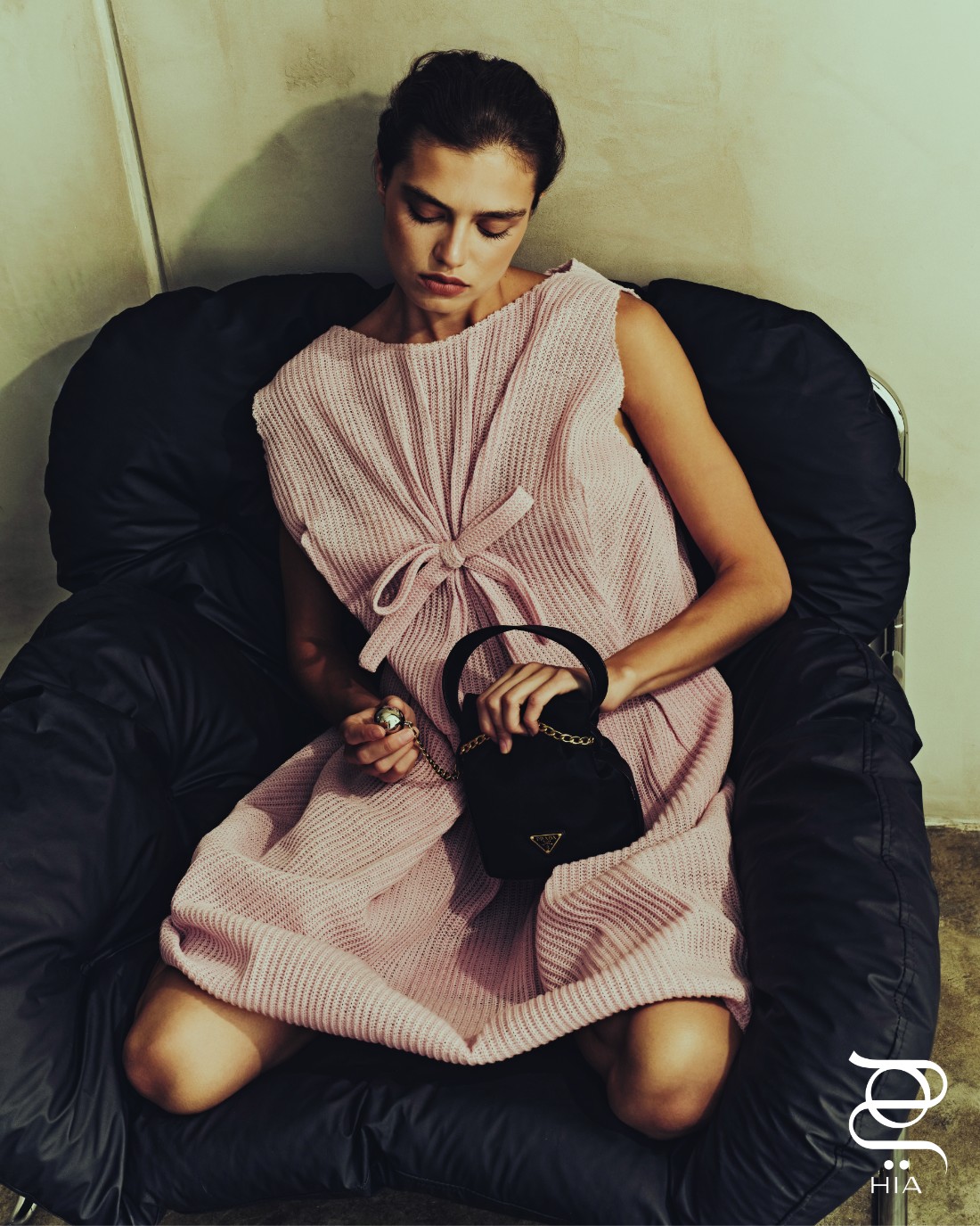فستان من الصوف، وحقيبة "بيتي ساك نوار" الدلو بالحجم الصغير Petit Sac Noir Mini Bucket، جميعها من "برادا" Prada