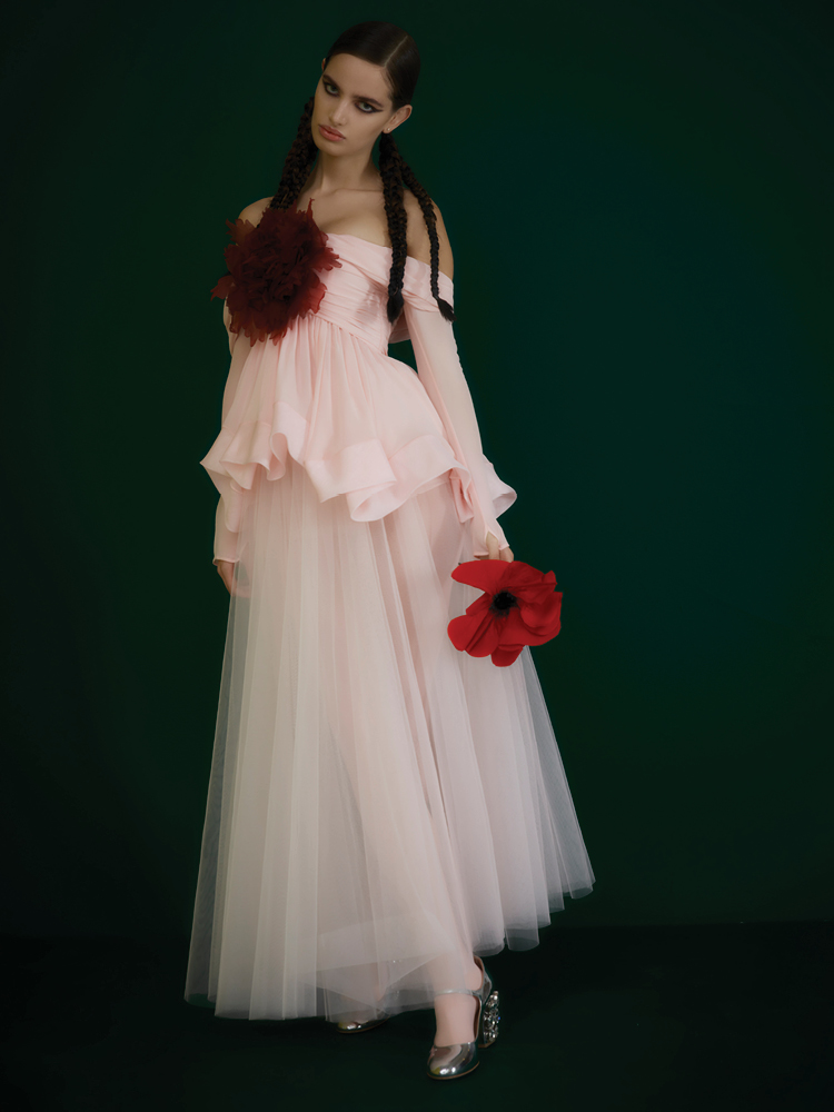 من "جامباتيستا فالي" Giambattista Valli، قميص وردي طويل الكمّين ومثني مع زهرة زينية موصولة، وتنورة وردية من التول، وجوارب وردية، وحذاء "ماري جين" فضي بكعب بلّوري.