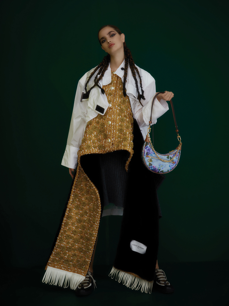 من "لويس فويتون" Louis Vuitton، فستان رمادي محبوك بشكل مضلّع، وقميص ذهبي موصول بوشاح من الفرو ذي وجهين، وسترة بيضاء صامدة ضد الماء، وحقيبة مطبّعة بالأزهار وبشعار الدار، وحذاء رياضي مفتوح الخلف.