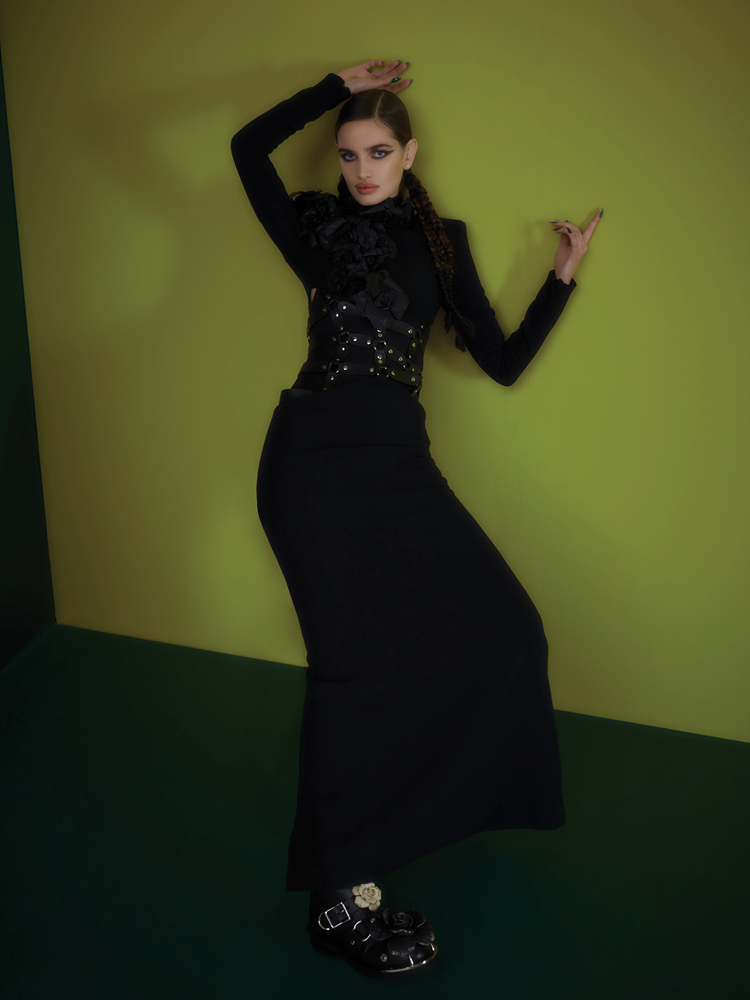 من "روبيرتو كافالي" Roberto Cavalli، فستان أسود طويل ذو أجزاء جلدية مقصوصة، فوقها زخرفات قماشية على شكل زهور، وجزمة عسكرية سوداء مزخرفة بأزهار متعددة الألوان. "بودي" أسود من خزانة المنسقة.