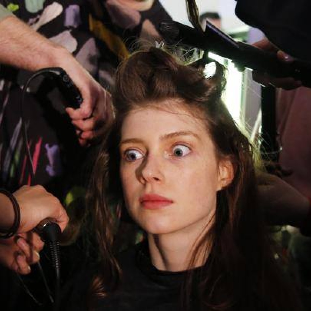 عارضة أزياء تبدو منبهرة أثناء تصفيف شعرها من قبل أكثر من خبير تجميل خلال عروض الأزياء في لندن!