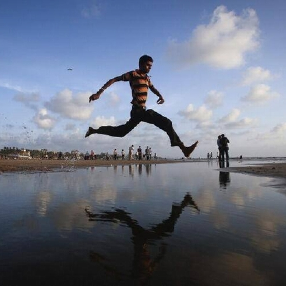 رجل يقفز فوق مياه متجمعة في شاطئ بحر العرب في الهند