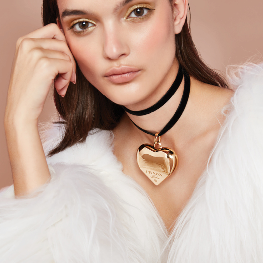 قطعة بيضاء من الفرو الصديق للبيئة والطويل الشعيرات من "برادا" Prada.  عقد "إيترنال غولد" Eternal Gold الضيّق ذو حلية ضخمة متدلية من الذهب الأصفر المعاد تدويره، وهو مصمم حسب الطلب من مجموعة المجوهرات الفاخرة من "برادا" Prada Fine Jewelry.