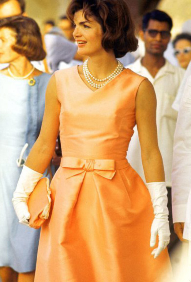 جاكي كندي بفستان أنيق مع عقدة على الخصر وعقد من اللؤلؤ وقفازات بيضاء