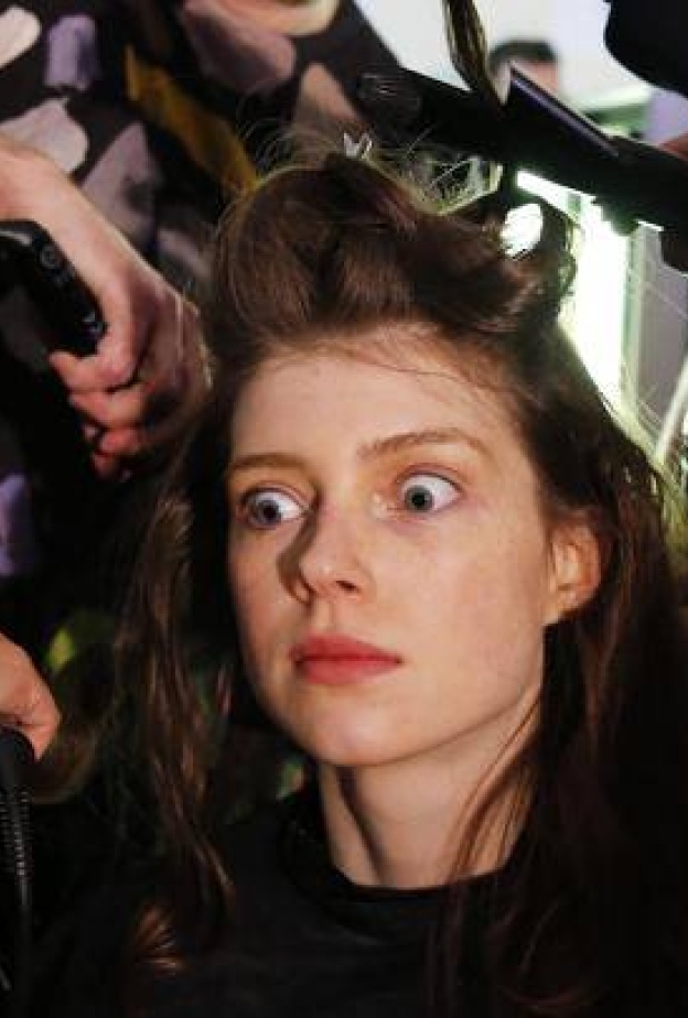 عارضة أزياء تبدو منبهرة أثناء تصفيف شعرها من قبل أكثر من خبير تجميل خلال عروض الأزياء في لندن!