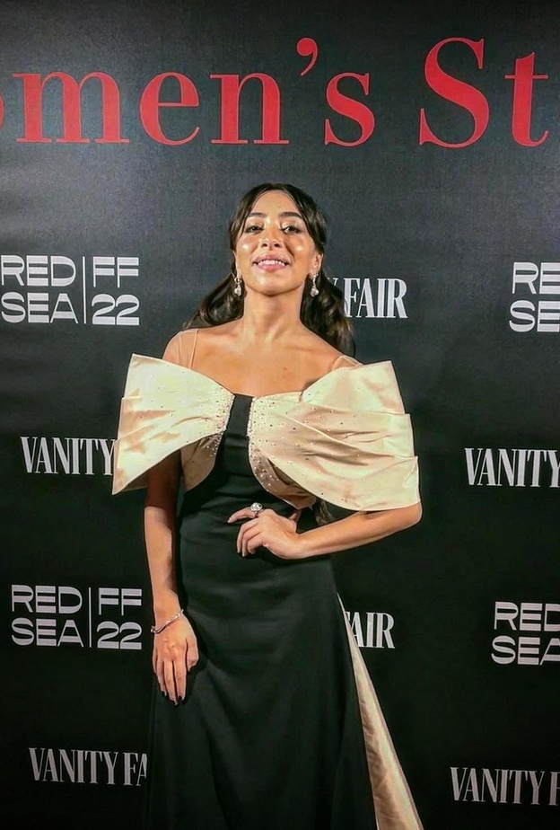 الممثلة السعودية سارة طيبة ترتدي فستانًا راقيًا باللون الأسود بأكتاف منسدلة باللون البيج من إلوستريلا في مهرجان البندقية السينمائي