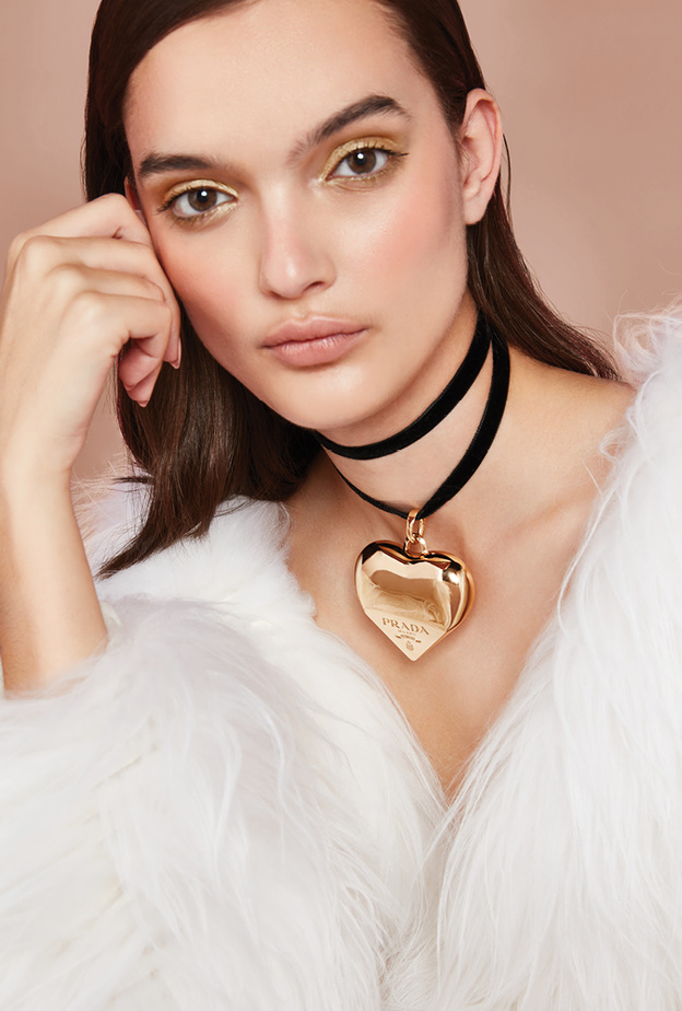 قطعة بيضاء من الفرو الصديق للبيئة والطويل الشعيرات من "برادا" Prada.  عقد "إيترنال غولد" Eternal Gold الضيّق ذو حلية ضخمة متدلية من الذهب الأصفر المعاد تدويره، وهو مصمم حسب الطلب من مجموعة المجوهرات الفاخرة من "برادا" Prada Fine Jewelry.