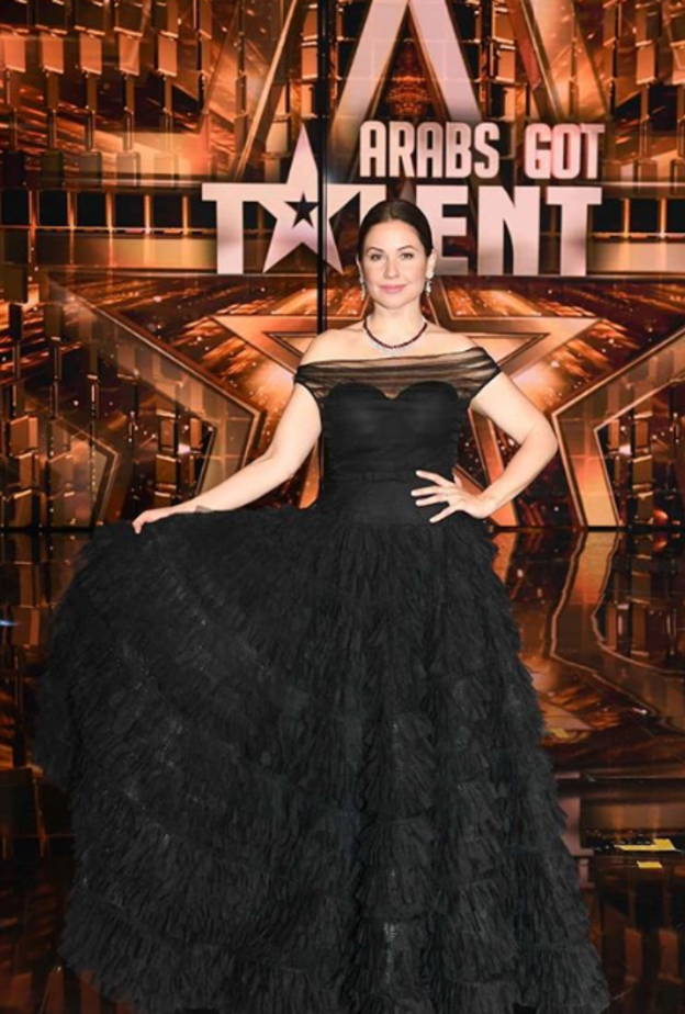 أطلت بفستان من تصميم نجا سعادة بقصة الكتف الواحد والكسرات كذلك الحزام المزيّن بالكريستالات والشق الجانبي