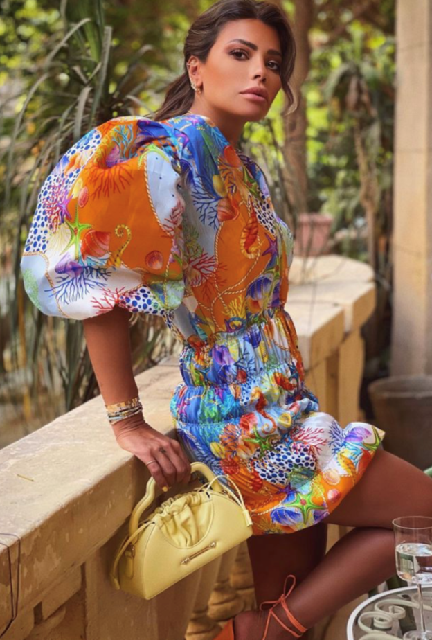 بدت بغاية الأناقة بالفستان القصير المنقوش نسّقت معه حقيبة باللون الأصفر من مجموعة OKHTEIN