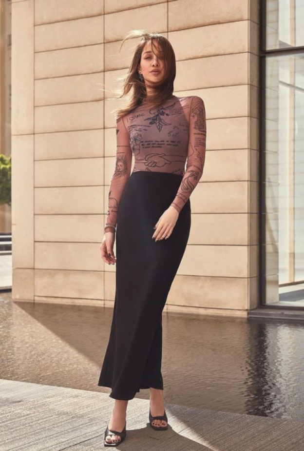 نسّقت التنورة الماكسي الضيقة بقصة الخصر العالي مع التوب الضيقة والمزيّنة بالرسمات والكتابات