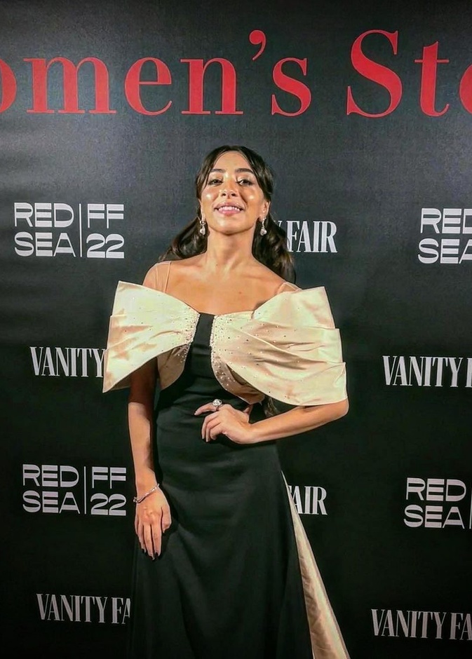 الممثلة السعودية سارة طيبة ترتدي فستانًا راقيًا باللون الأسود بأكتاف منسدلة باللون البيج من إلوستريلا في مهرجان البندقية السينمائي