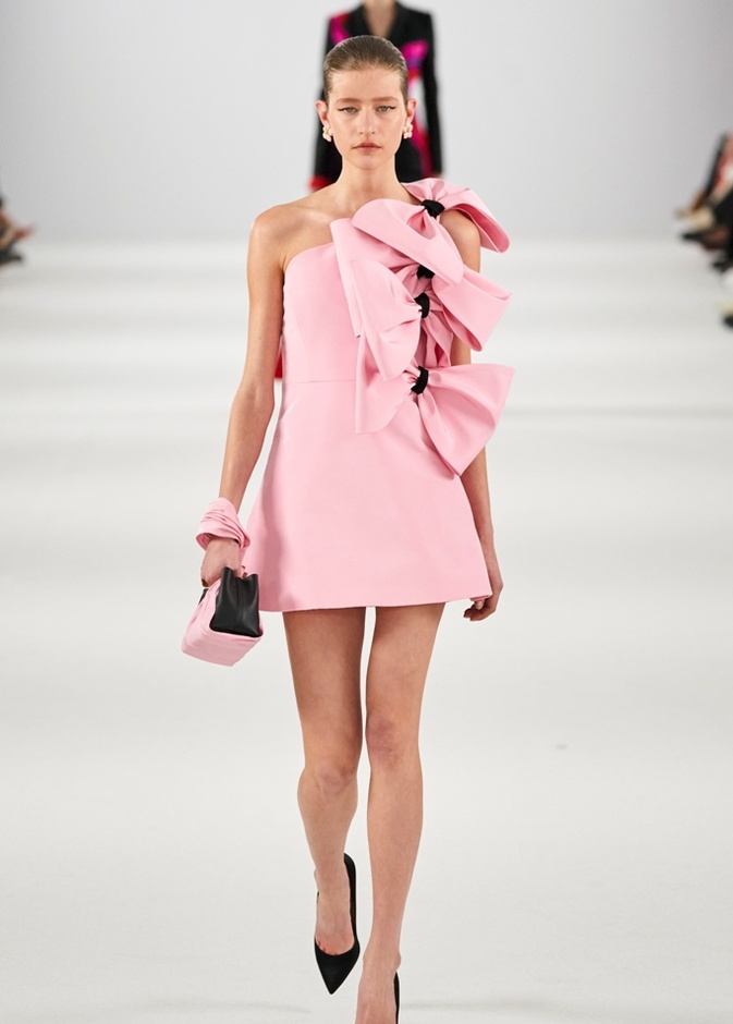 فستان وردي قصير مزين بعقد كبيرة، وحذاء أسود بقصة منخفضة، وحقيبة صغيرة باللونين الأسود والوردي من كارولينا هيريرا 