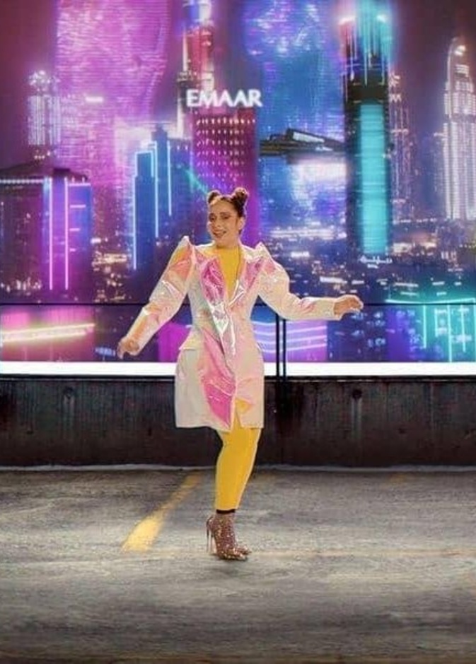 أطلت باللون الأصفر ونسّقت فوقه المعطف الميدي بقماش ميتاليكي وبألوان قوس القزح المتغيّرة