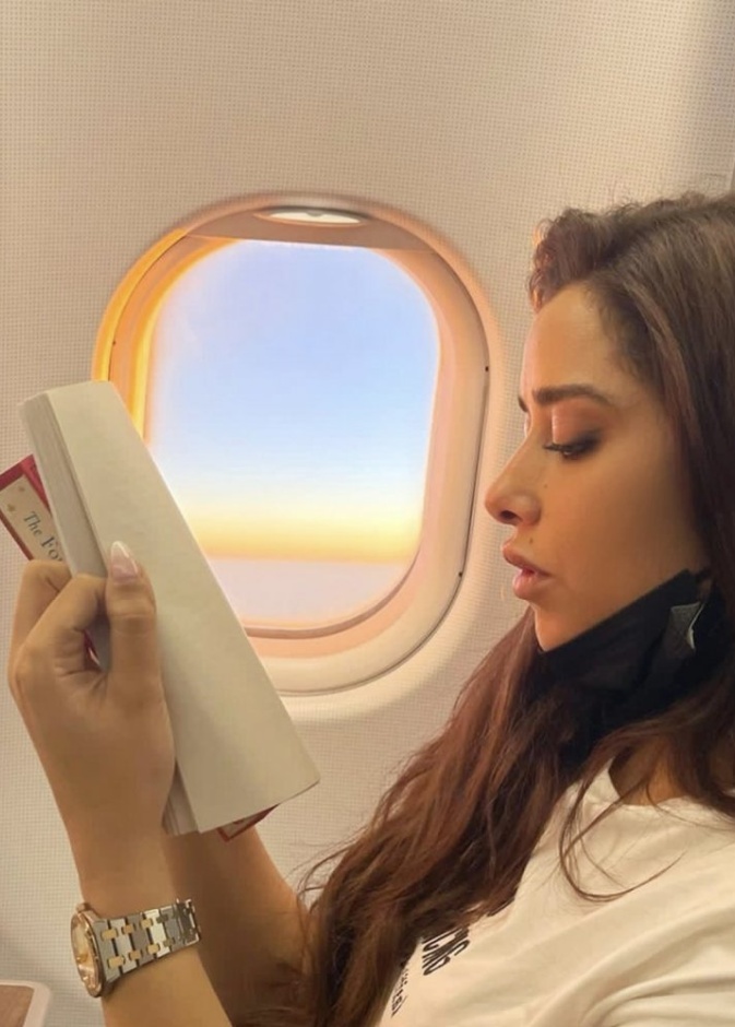 بلقيس فتحي تستمتع بقراءة كتابها الجديد خلال رحلتها في الطائرة