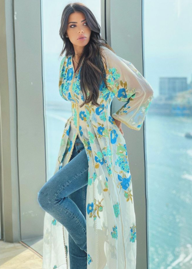 نسقت القفطان الأبيض الذي تميّز بقماشه الشفاف والمزيّن بالورود الزرقاء مع البنطلون الدنيم