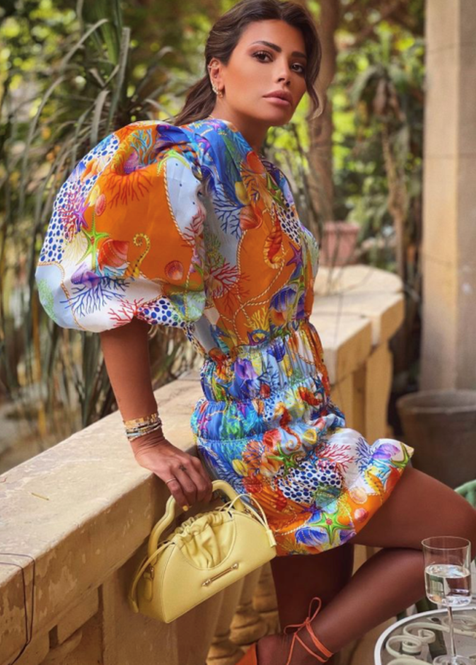 بدت بغاية الأناقة بالفستان القصير المنقوش نسّقت معه حقيبة باللون الأصفر من مجموعة OKHTEIN