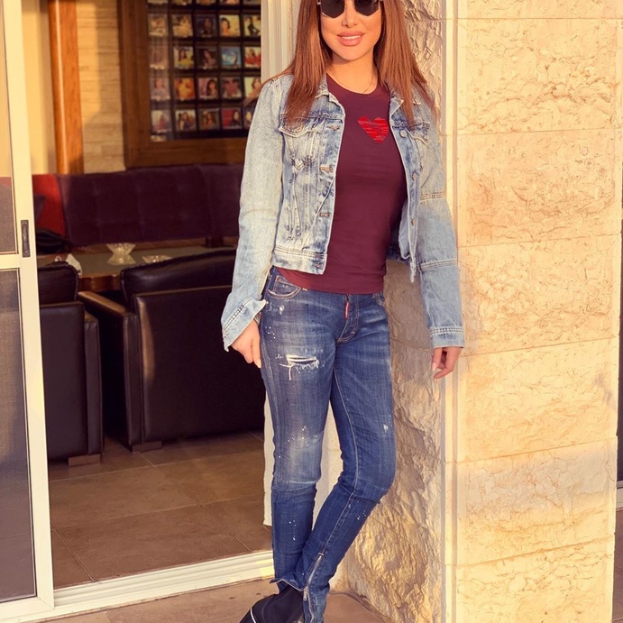 تألقي بأسلوب نجوى كرم بموضة بنطلون الجينز الضيق بلونه الداكن مع بعد الخيوط البيضاء الممزقة ونسّقيه مع التوب الضيقة وجاكيت الجينز المستقيمة بلونها الفاتح.