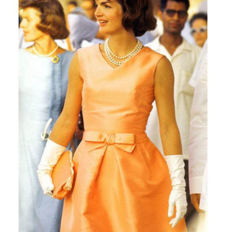 جاكي كندي بفستان أنيق مع عقدة على الخصر وعقد من اللؤلؤ وقفازات بيضاء