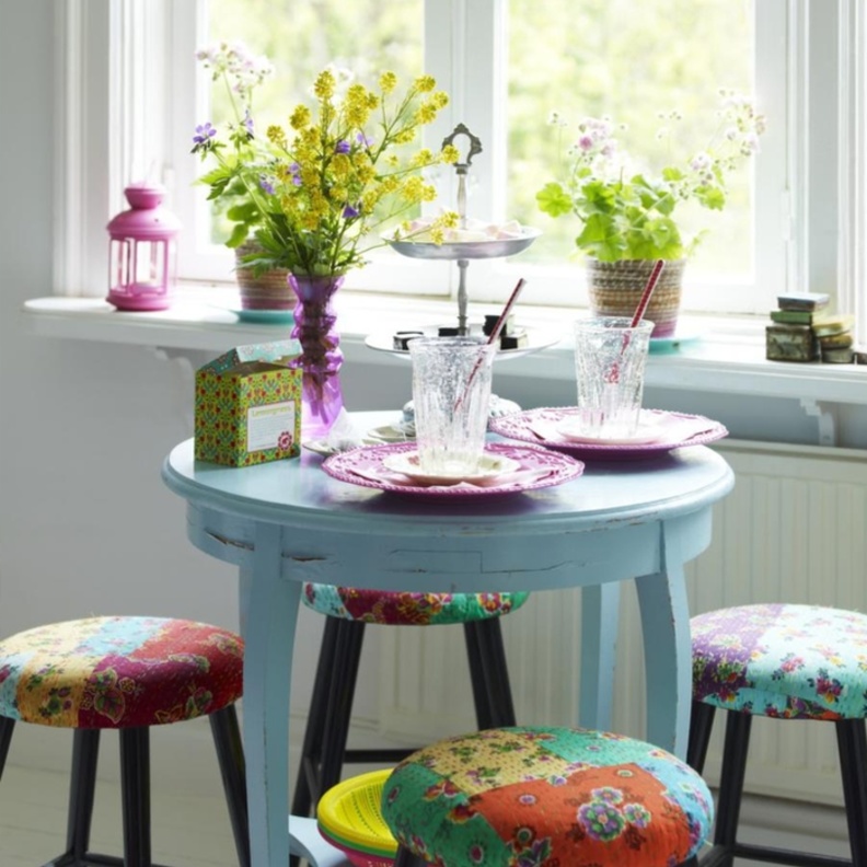 طاولة صغيرة بدرجة فاتحة من الأزرق مع كراسٍ بسيطة منجدة بألوان متفاوتة على الطراز الهندي