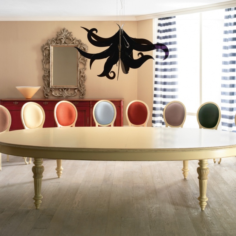 طاولة ذات شكل بيضاوي باللون الكريمي وعدد هائل من الكراسي الملونة بألوان مختلف