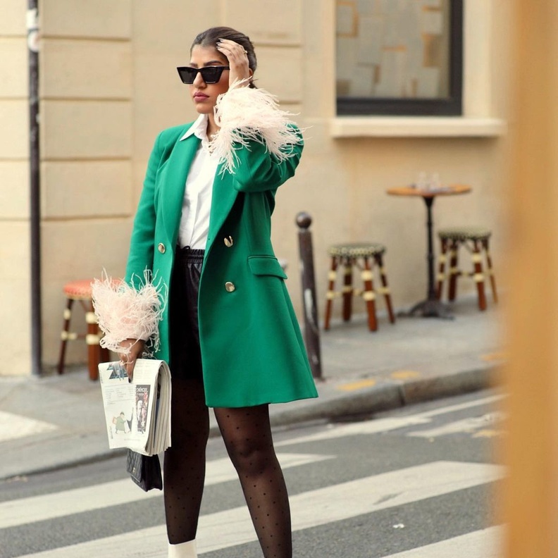 أطلت بالقميص الأبيض نسّقت معه الشورت الجلد القصير والمعطف الأخضر