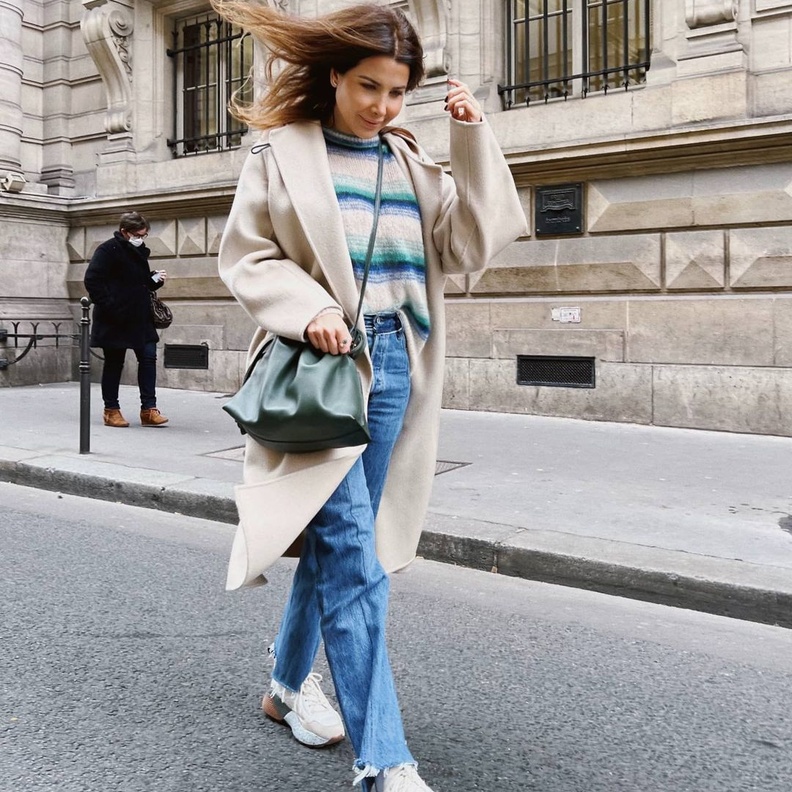 نسّقت مع البنطلون الدنيم الأزرق الكنزة باللونين الأبيض والأزرق وأكملت اللوك بالمعطف البيج الميدي