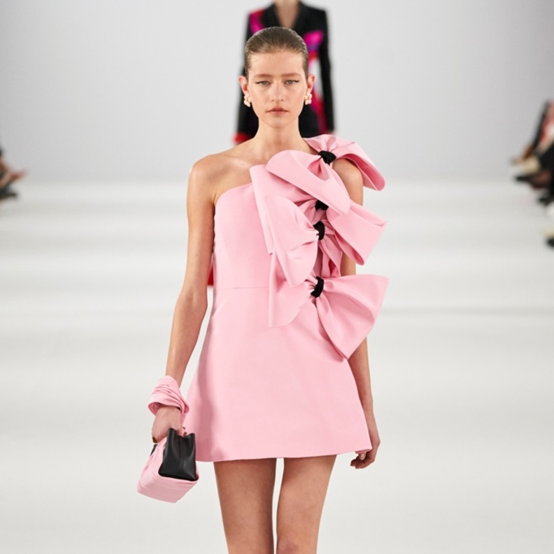 فستان وردي قصير مزين بعقد كبيرة، وحذاء أسود بقصة منخفضة، وحقيبة صغيرة باللونين الأسود والوردي من كارولينا هيريرا 