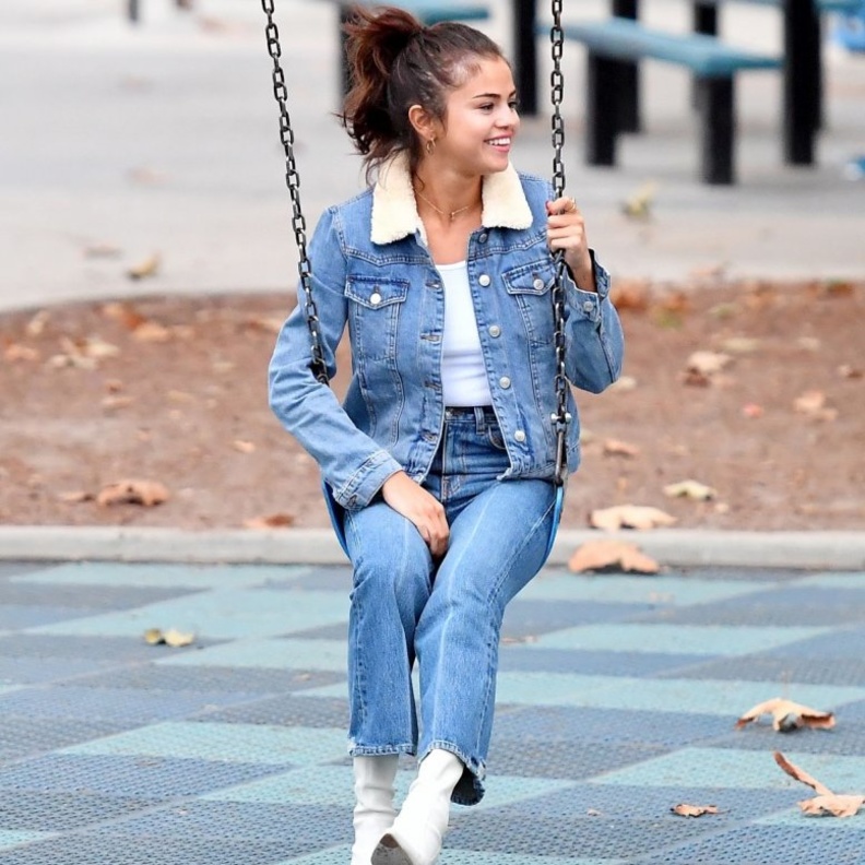 لوك صباحي اختارت فيه سيلينا غوميز معطف طويل باللون الرمادي ونسقته مع حذاء أبيض وشنطة يد من كوتش