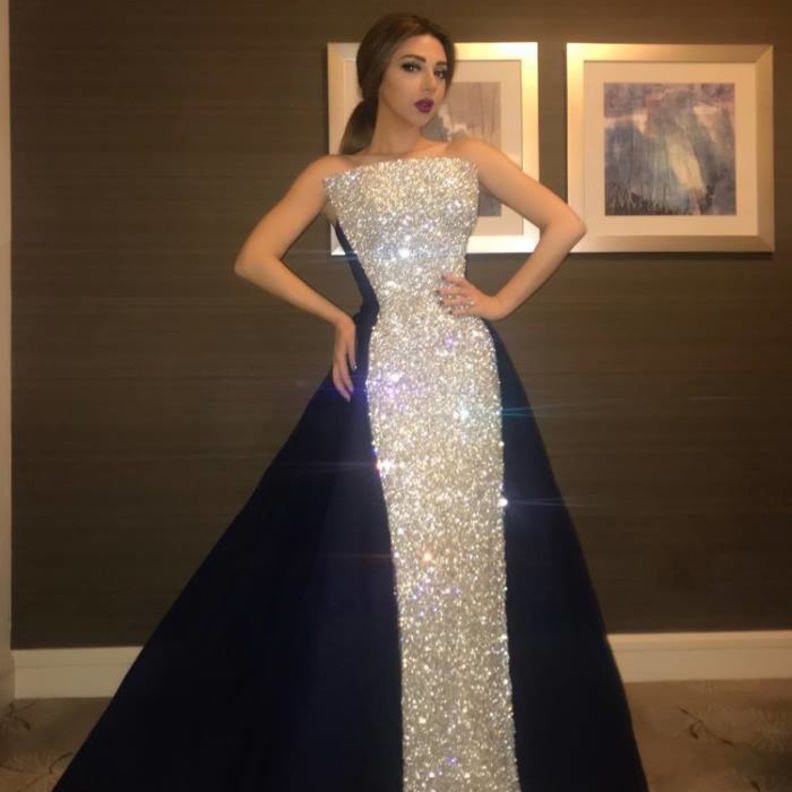 جمع الفستان بين قماشين الاول فضيّ برّاق والثاني جاء باللون الكحلي من الخلف وعند الجانبين