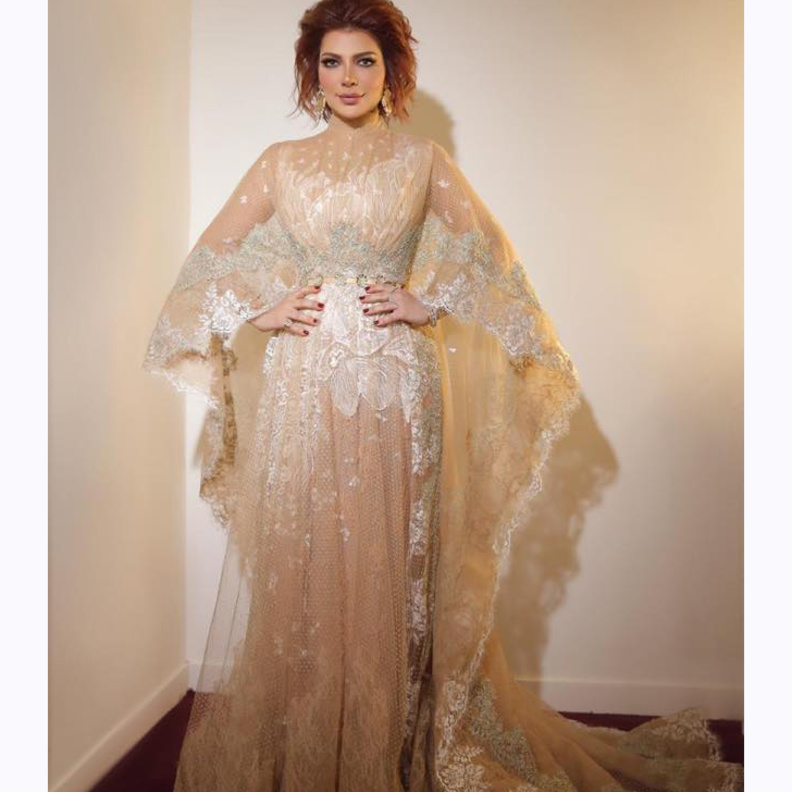  الفستان جاء بياقة عالية، وبأكمام واسعة كالكاب فإنسدلت بإنسيابية على الأرض