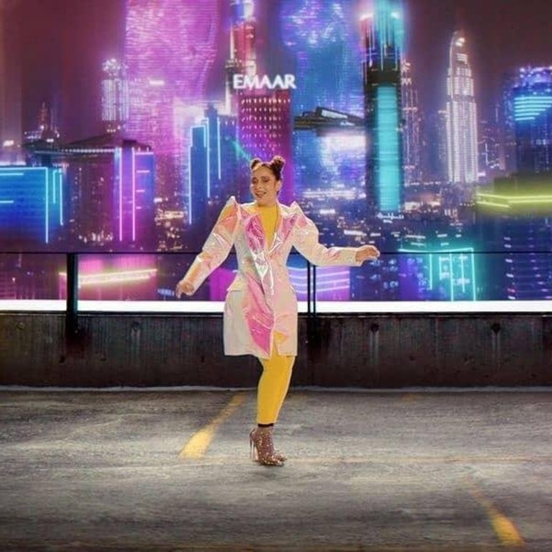 أطلت باللون الأصفر ونسّقت فوقه المعطف الميدي بقماش ميتاليكي وبألوان قوس القزح المتغيّرة