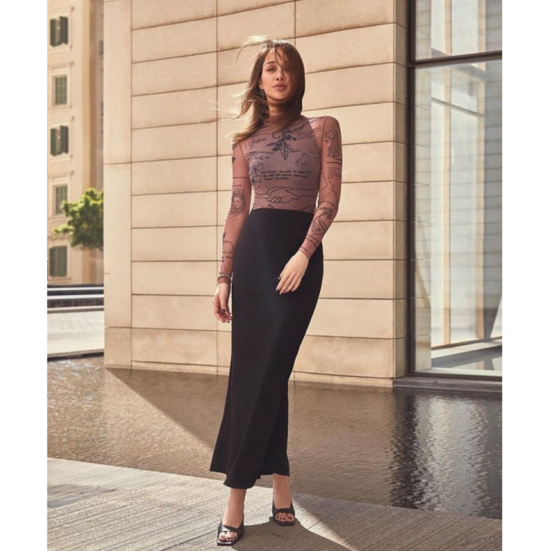 نسّقت التنورة الماكسي الضيقة بقصة الخصر العالي مع التوب الضيقة والمزيّنة بالرسمات والكتابات