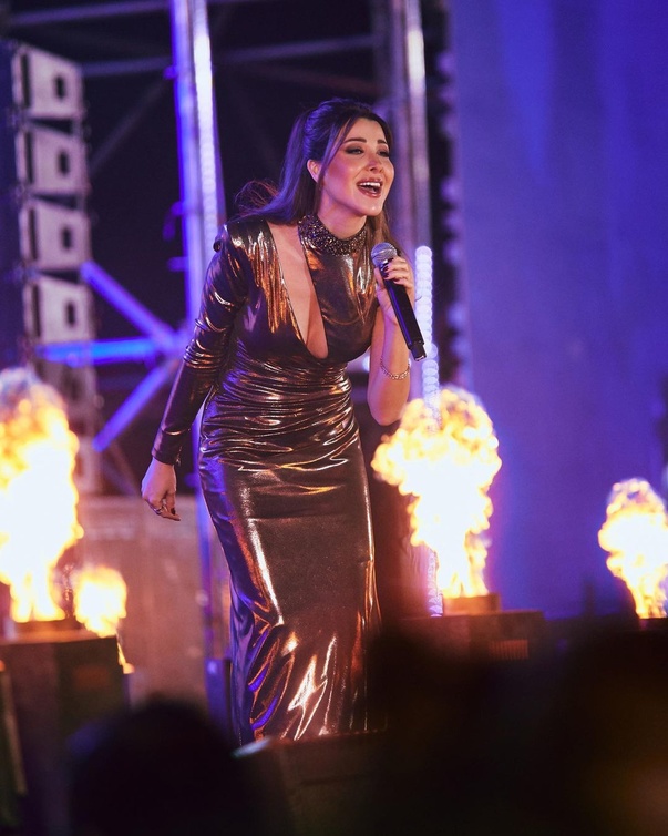 نانسي عجرم بفستان برونزي طويل بكم وحيد مع ياقة عالية مرصعة مزينة بفتحة مائلة